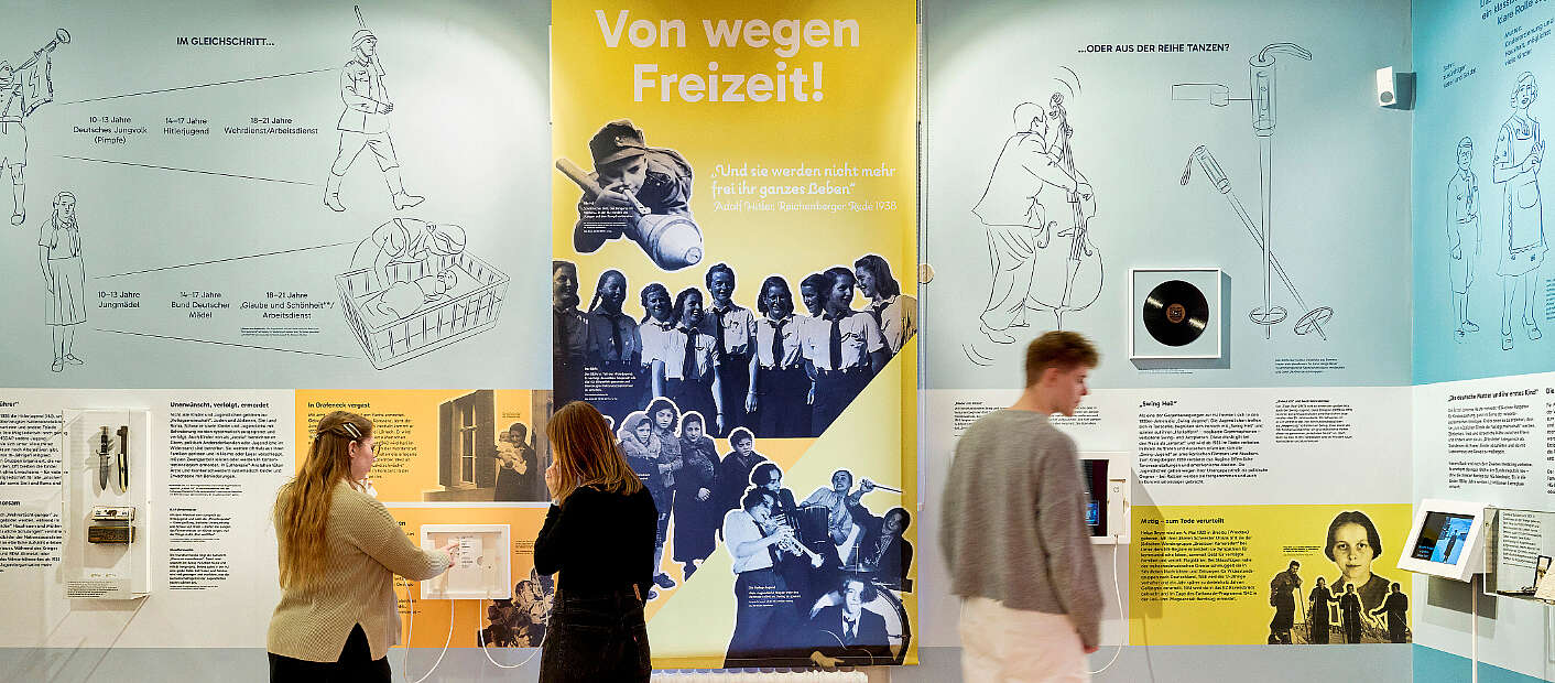 Drei Jugendliche schauen sich Ausstellungswände an.