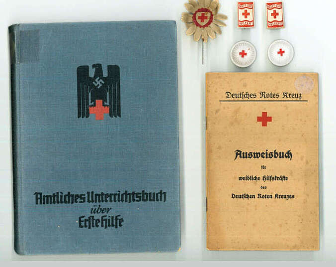 Ein blaues Buch mit dem Titel "Amtliches Unterrichtsbuch über Erste Hilfe", ein hellbraunes "AUsweisbuch für weibliche Hilfskräfte des Deutschen Roten Kreuzes" und fünf Abzeichen des WInterhilfswerk, die alle das Logo des Roten Kreuzes tragen, liegen nebeneinander.