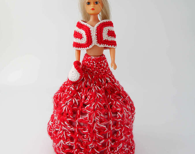 Eine Barbiepuppe in einem roten gehäkelten Kleid. Unter Ihrem Rock ist eine Rolle pinkfarbenes Klopapier.