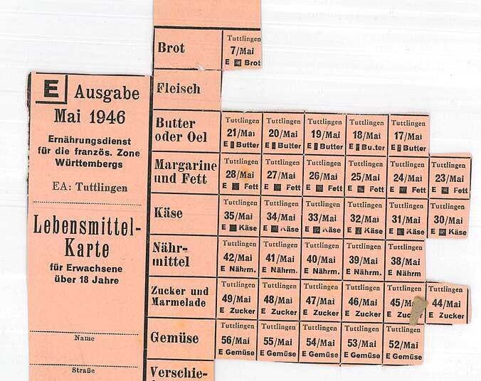 Eine pinke Lebensmittelkarte. Beschriftet ist sie mit:"Ausgabe Mai 1946". Mehrere Lebensmittelmarken sind herausgeschnitten worden.