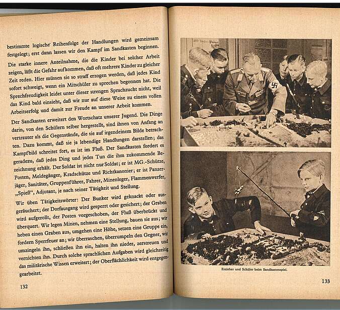 Eine Doppelseite des "Sandkastenhandbuch." auf ihr ist ein Foto von Schülern in HJ-Uniform und erwachsenen Männern in Wehrmachtsuniform zu sehen, wie sie um einen Sandkasten herum stehen.