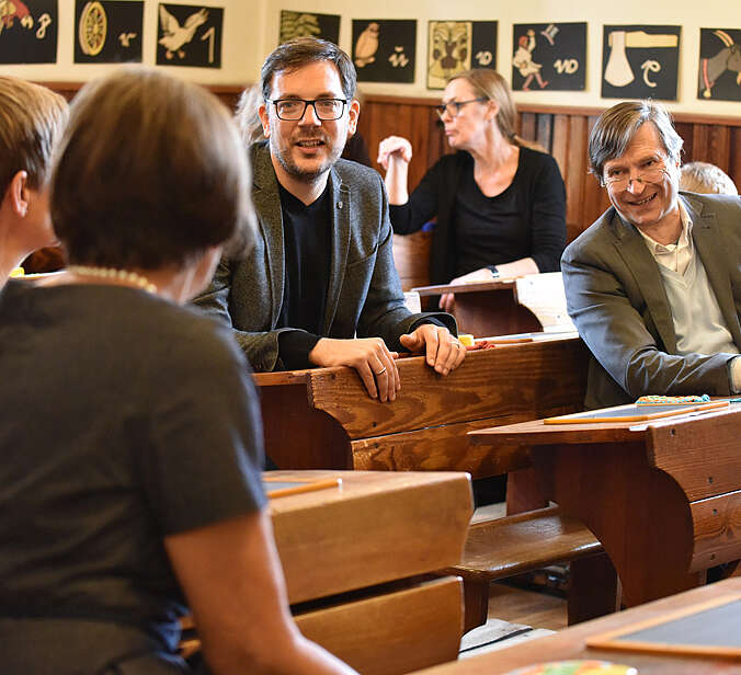 Besucher unterhalten sich auf den alten Schulbänken