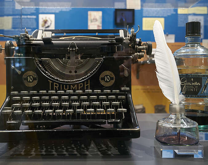 Alte mechanische Triumph-Schreibmaschine neben Federkiel und Tintenglas
