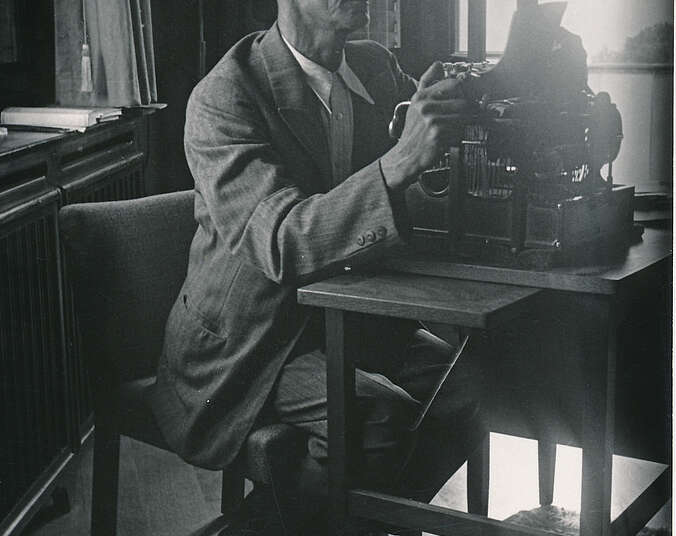 Schwarz-weiß-Foto: Mann sitzt an alter Schreibmaschine