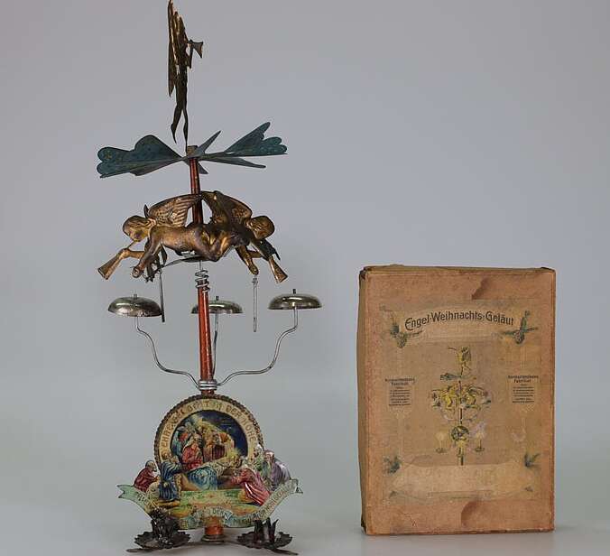 Ein aufgebautes Engelsgeläut aus Blech. Danaben sthet eine Verpackung aus Pappe für ein Engelsgeläut.