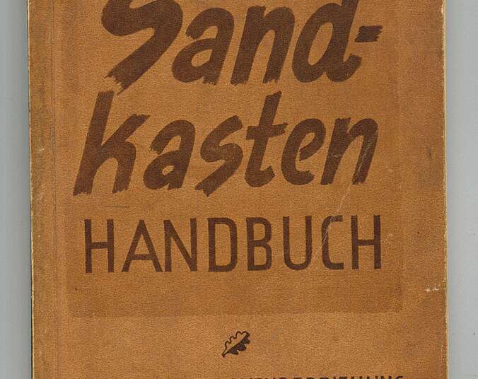 Die Titelseite eines braunen Buches. In dunkelbraunen Buchstaben steht darauf "Sandkastenhandbuch. Ein Beitrag zur Wehrerziehung der Schuljugend."