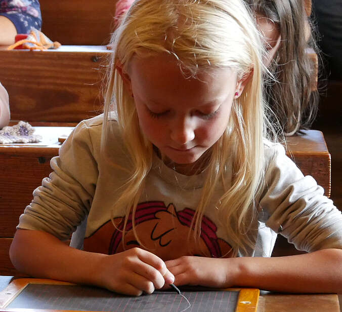 Mädchen schreibt mit Griffel auf Schiefertafel