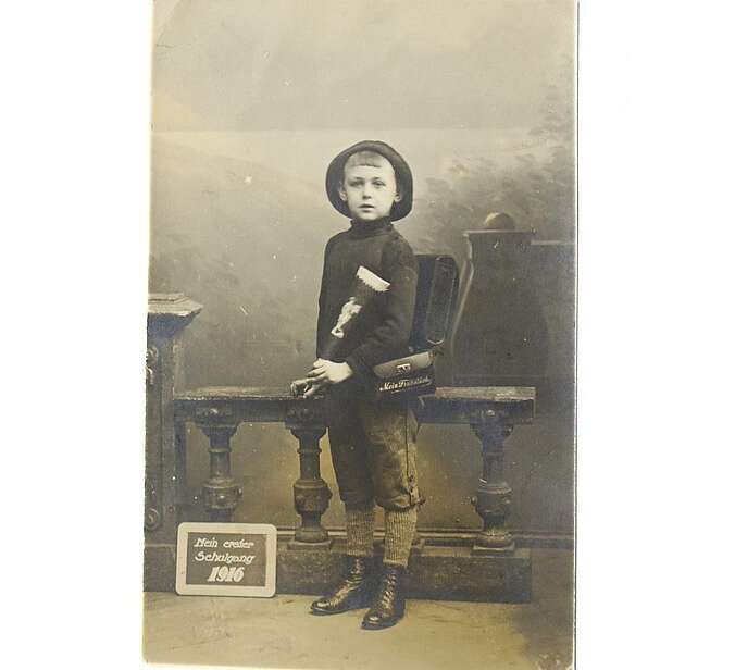 Ein Foto eines Jungen von 1916. Er hat eine Frühstückstasche um.