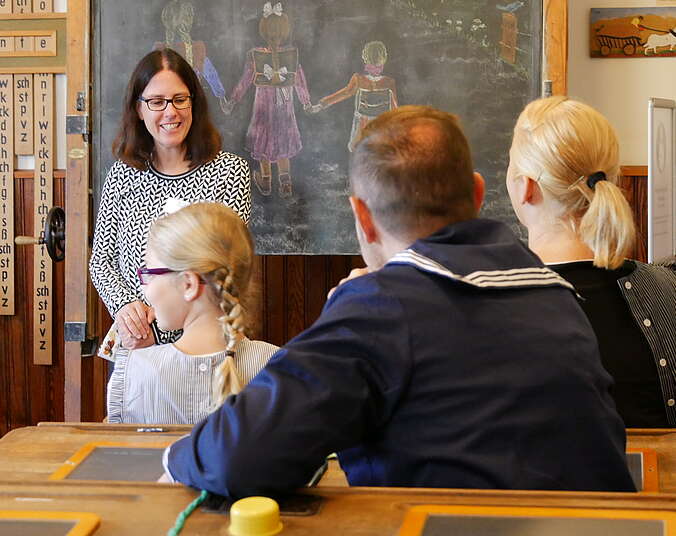 Eine Museumsführerin zeigt Besuchern ein altes Klassenzimmer